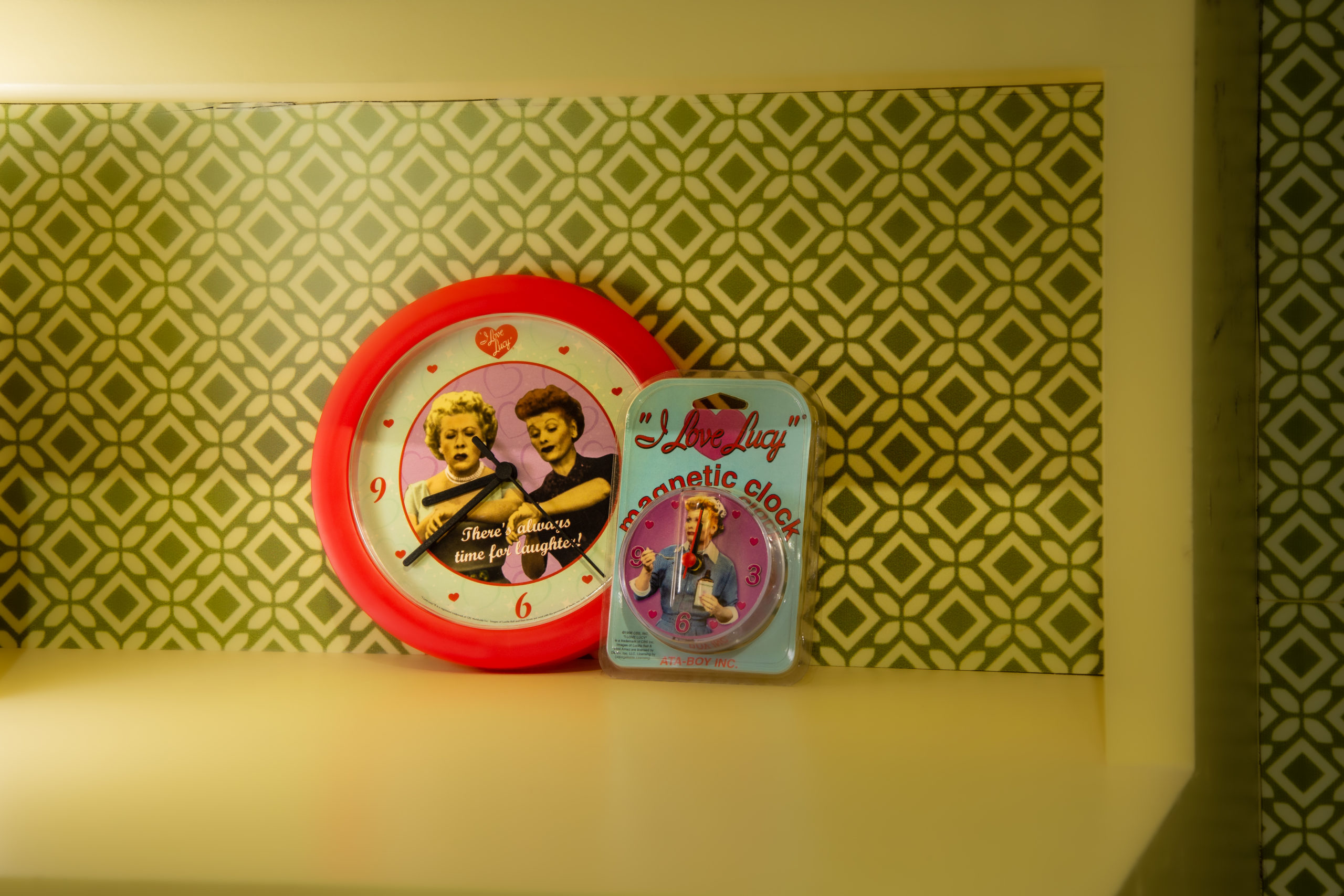 Two I Love Lucy themed clocks on display in front of vintage wallpaper